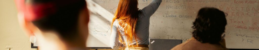 Female teacher writing complex formulas on a whiteboard during a university lecture.